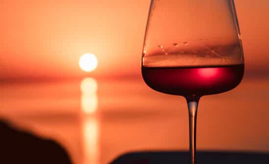 Glas Rotwein im Abendlicht während eines Sonnenuntergangs