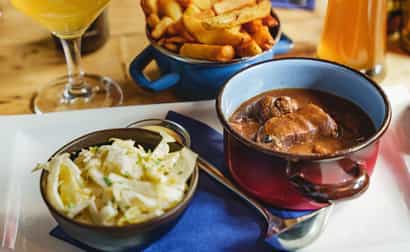 Traditionelles belgisches Gericht mit Gulasch, knusprigen Pommes, Krautsalat und einem Glas Bier auf einem Holztisch