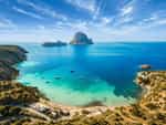 Traumhafter Blick auf die Bucht von Cala d’Hort auf Ibiza mit türkisblauem Meer, felsiger Küstenlandschaft und der beeindruckenden Felsinsel Es Vedrà im Hintergrund.