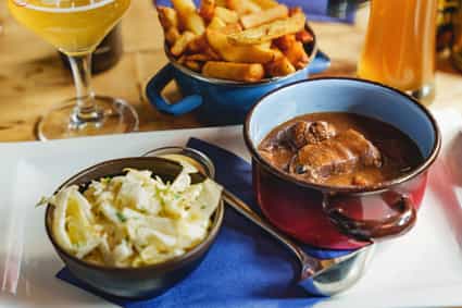 Traditionelles belgisches Gericht mit Gulasch, knusprigen Pommes, Krautsalat und einem Glas Bier auf einem Holztisch