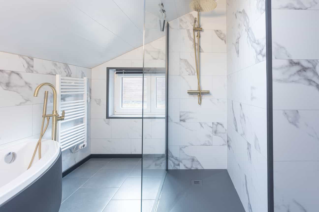 Stilvolles, minimalistisches Design-Badezimmer mit integrierter Badewanne, Glasdusche und weißer Wandverkleidung in Steinoptik.