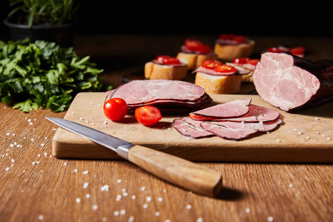 Scheiben von Ardenner Schinken auf Baguette-St�ücken, serviert auf Holzbrett mit Kirschtomaten im Hintergrund