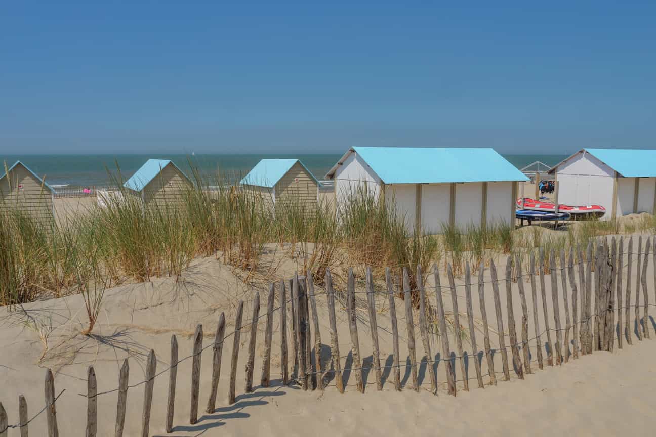 Sandstrand an der belgischen Küste mit Holzhüttchen, Dünengras und typischen Holz-Sandzäunen