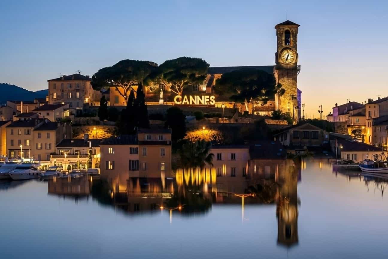Cannes bei Nacht mit beleuchteter Kirche, Stadtlichtern und Spiegelungen im Meer an der Côte d’Azur