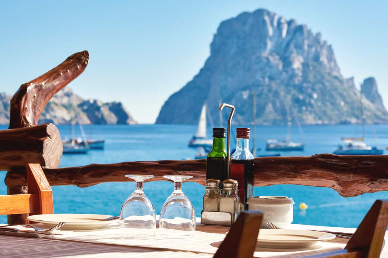 Außenrestaurant auf Ibiza mit Terrasse und Blick auf die Felseninsel Es Vedrà im Meer