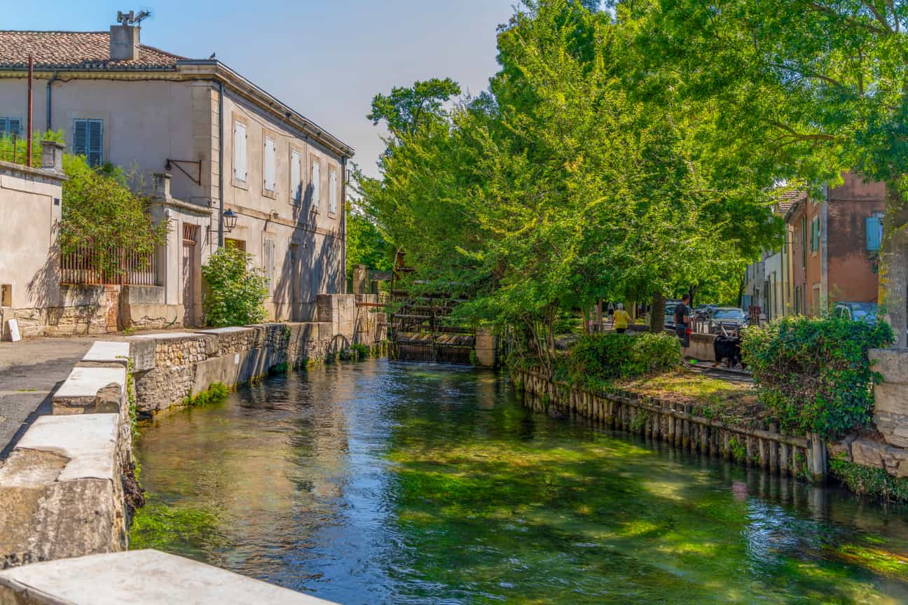 Stimmungsvolle Ansicht von L’Isle-sur-la-Sorgue mit Wasserlauf, alten Gebäuden und grüner Umgebung in Südfrankreich