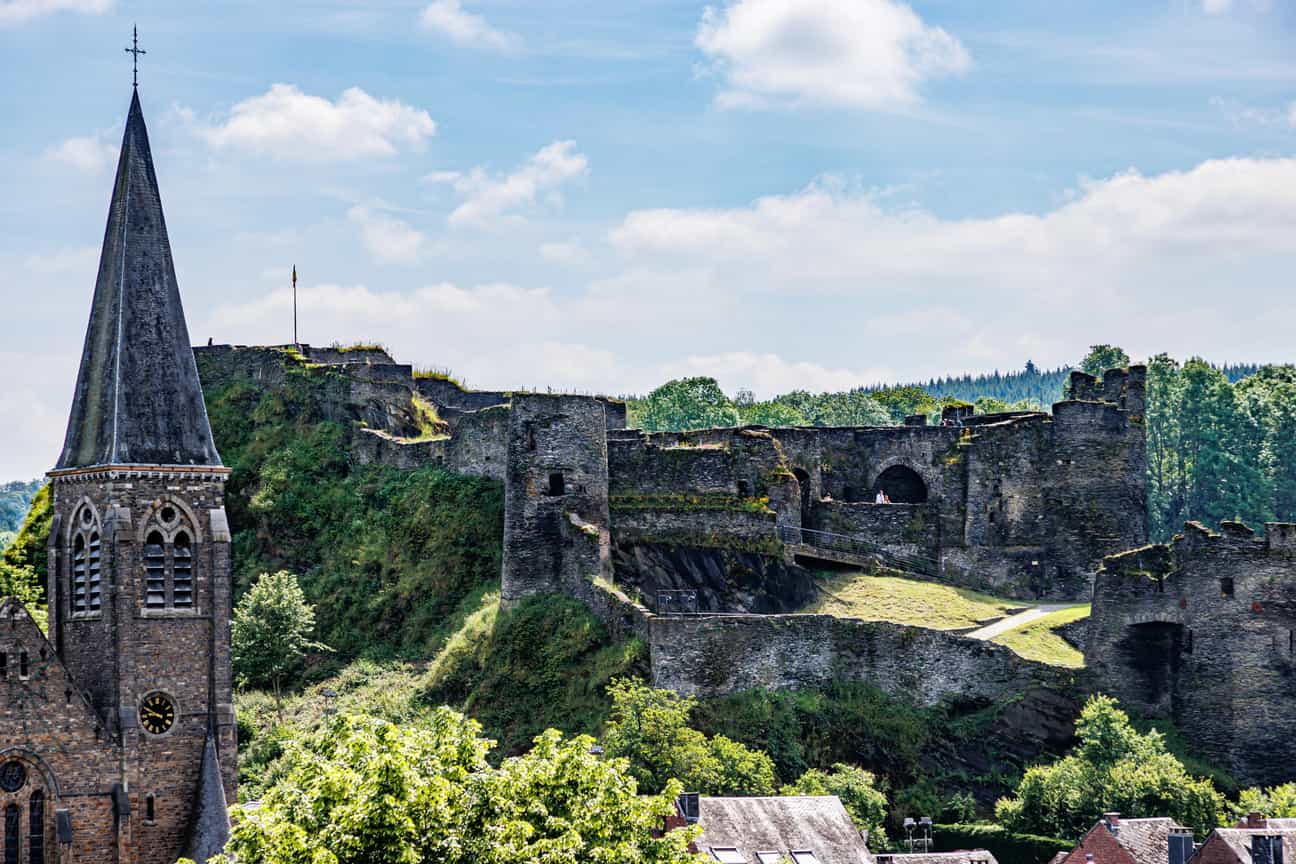 Luftaufnahme der Burgruine La Roche-en-Ardenne und der St.-Nikolaus-Kirche, umgeben von Wald und Vegetation