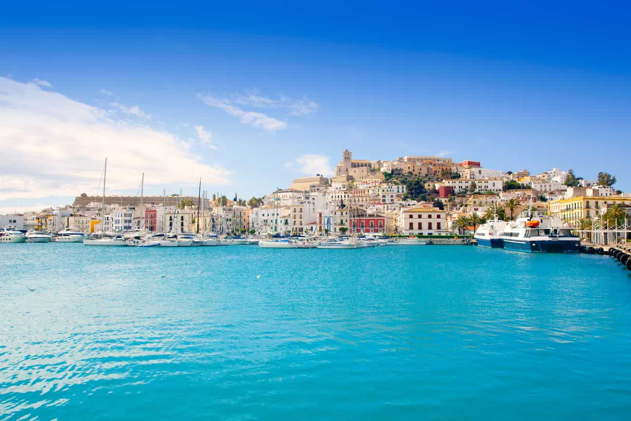 Panoramablick auf Ibiza-Stadt mit dem Hafen, zahlreichen Booten und Schiffen im Mittelmeer sowie der Stadtlandschaft im Hintergrund.