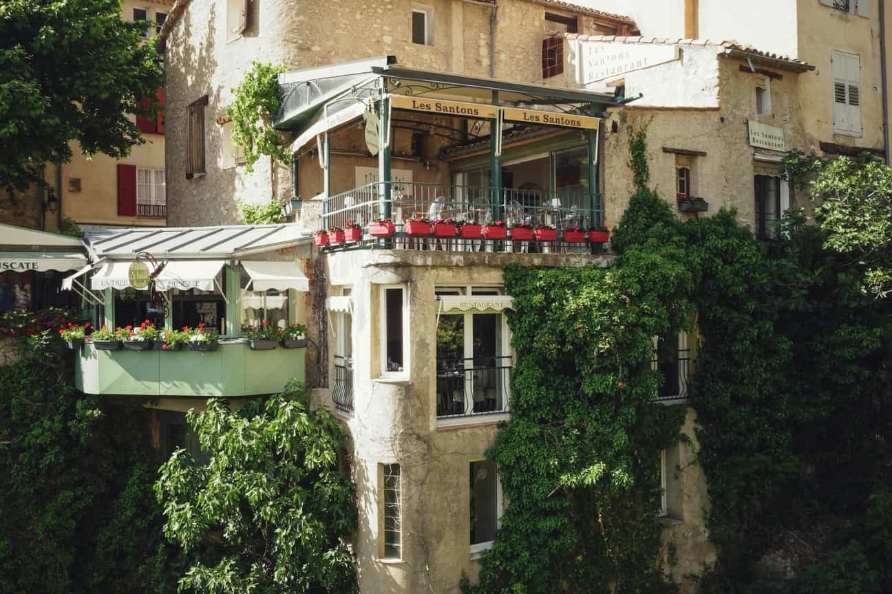 Blick über die Schlucht von Moustiers-Sainte-Marie auf ein Restaurant, das malerisch an den Felsen gebaut ist