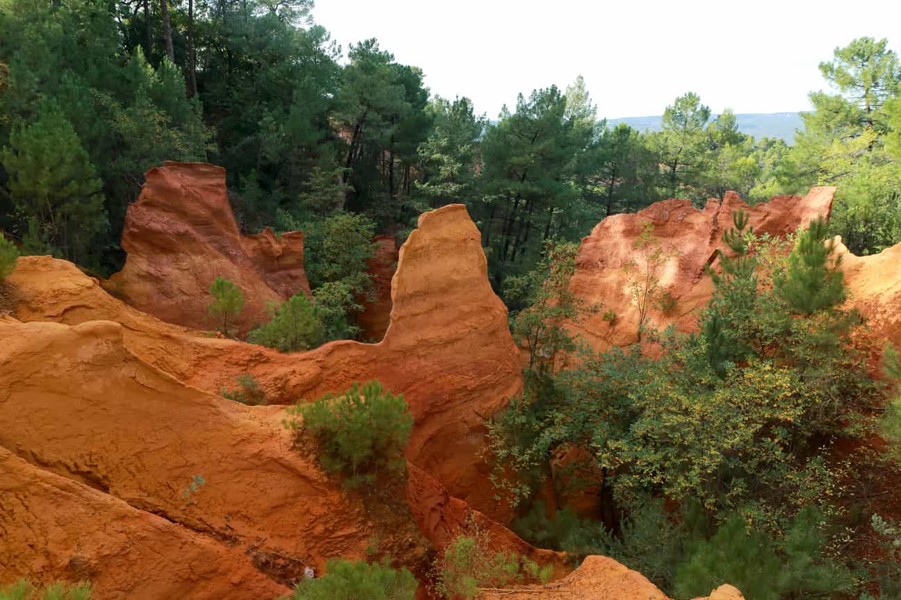 Ockerfarbener Wanderweg bei Roussillon mit Bäumen und rötlichen Felsen in der Provence