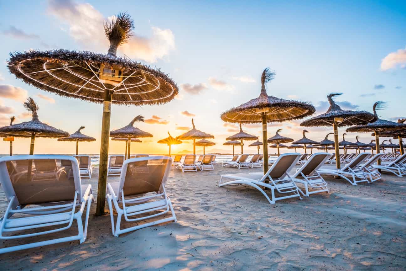 Alt-Text: Strand von Playa de Muro auf Mallorca bei Sonnenaufgang mit Liegen im Vordergrund