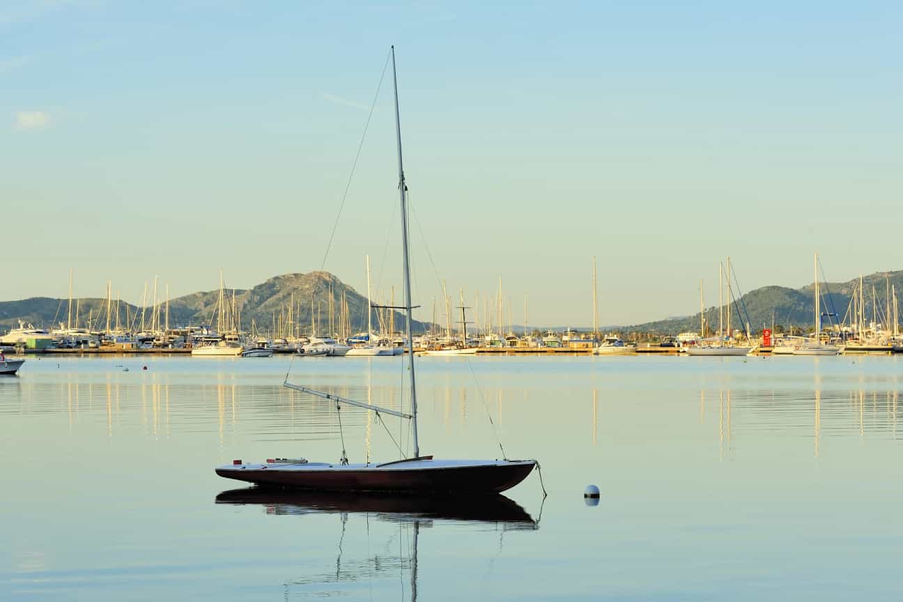 Ein Segelboot mit eingeklappten Segeln liegt ruhig im Hafen von Mallorca in der Morgensonne