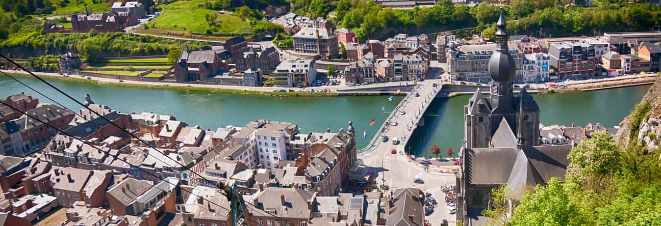 Panoramablick über die belgische Stadt Dinant mit Fluss, Altstadt und umgebender Hügellandschaft.