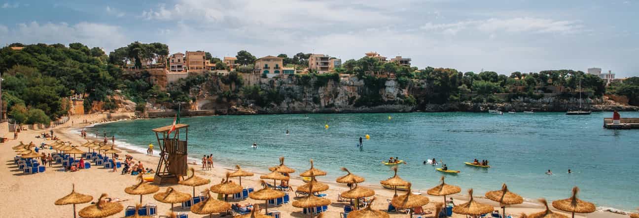 Strand von Porto Cristo auf Mallorca mit Wasser, Strandstühlen und Stadt im Hintergrund
